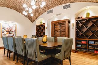 A stylish dining area features a large wooden table, upholstered chairs, a vintage door, and wine storage, all beneath a curved brick ceiling.