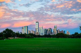 A vibrant skyline at sunset, with colorful clouds reflecting above a lush green park, creating a serene urban landscape.