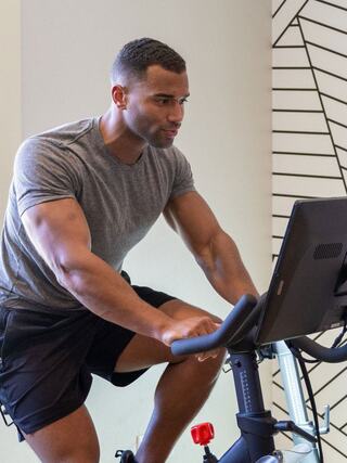 A focused man is engaged in an indoor cycling workout, showcasing determination and strength. The setting features modern decor.