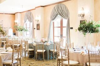 Elegant banquet hall with round tables set for an event, adorned with greenery and soft drapes, creating a refined atmosphere.