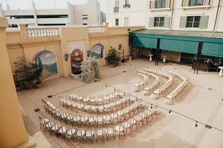 An outdoor wedding venue features rows of elegant chairs, floral arrangements, and a decorative backdrop under a sunny sky.
