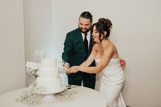 A couple joyfully cuts their wedding cake together, surrounded by delicate floral decor, capturing a moment of celebration and love.