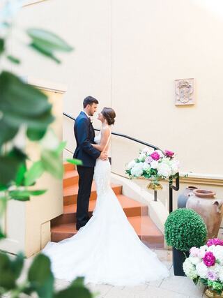 A couple shares an intimate moment on a staircase, surrounded by lush greenery and elegant floral arrangements, celebrating their love.