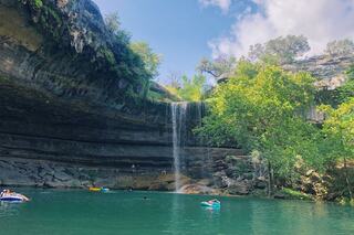 A serene waterfall cascades into a clear, emerald pool, surrounded by lush greenery and rocky cliffs, inviting outdoor enthusiasts.