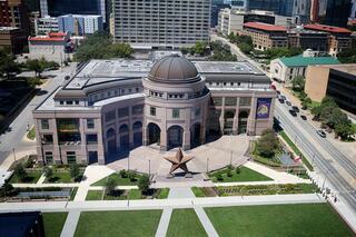A modern building features a large dome and a prominent star sculpture in a green plaza, surrounded by urban architecture and streets.
