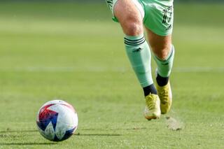 A player in green shorts kicks a soccer ball on a grassy field, showcasing dynamic movement and athletic focus.