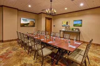 A meeting room features a large table surrounded by chairs, with a chandelier above and floral decor, creating a professional atmosphere.