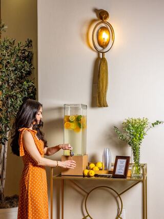 A woman in a polka dot dress serves refreshing fruit-infused water from a stylish dispenser, surrounded by lemons and greenery.