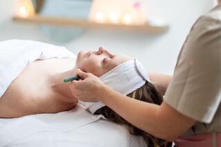 A woman relaxes during a spa treatment, while a therapist uses a tool on her face, surrounded by soft lighting and a serene atmosphere.