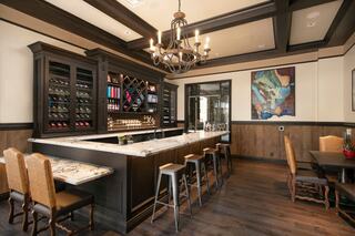 A stylish bar area features a marble countertop, wooden cabinetry, and elegant seating, set against warm tones and tasteful artwork.
