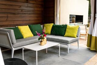 A cozy outdoor lounge area features a modern sofa with vibrant green and yellow cushions, a sleek coffee table, and potted flowers.