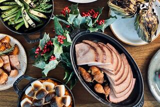 A festive spread features sliced ham, roasted vegetables, and flavorful sides, garnished with holly berries for a holiday touch.