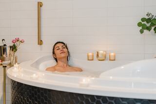 A woman relaxes in a luxurious bath, surrounded by candles and flowers, exuding a serene, tranquil ambiance.