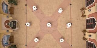 A spacious courtyard with a fountain at the center, surrounded by tables and chairs, features decorative lighting and vibrant architecture.