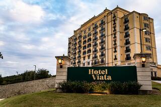 A stylish building with a mixture of modern and classic architecture, featuring "Hotel Viata" signage surrounded by greenery and a cloudy sky.