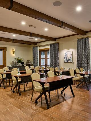 A well-lit meeting room with wooden beams, arranged tables, and chairs, featuring floral decor and a cozy atmosphere.