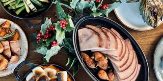 A festive spread features glazed ham, roasted vegetables, and seasonal greenery, evoking a warm, celebratory atmosphere.