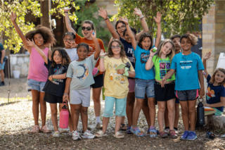 A cheerful group of girls waves and smiles, enjoying a sunny day outdoors, showcasing friendship and fun in a lively gathering.