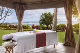 A serene outdoor massage setting overlooking the ocean, surrounded by lush greenery, inviting relaxation and tranquility.