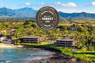 A coastal scene features beachfront resorts amid lush palm trees, with majestic mountains in the background under a bright blue sky.