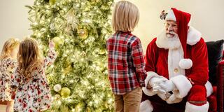 A festive scene features children interacting with Santa Claus beside a beautifully decorated Christmas tree. Joy and wonder fill the atmosphere.