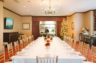 An elegant dining room features a long table set with festive décor, a chandelier, and a Christmas tree, creating a warm atmosphere.