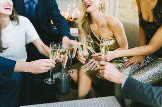 A group of elegantly dressed people joyfully toasting with champagne flutes, surrounded by a cozy ambiance and lively laughter.