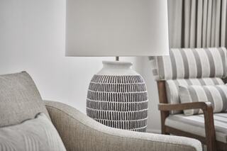 A cozy interior featuring a textured armchair, a patterned lamp, and a stylish striped sofa, creating a warm, inviting atmosphere.