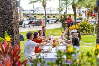 A group of friends enjoys a joyful toast at a beautifully decorated outdoor table, surrounded by vibrant flowers and tropical scenery.
