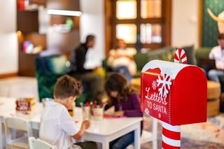 A cheerful scene with kids at a table crafting letters to Santa, alongside a festive mailbox for their messages in a cozy setting.