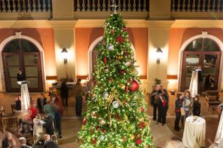 A beautifully decorated Christmas tree sparkles in a festive setting, with guests mingling and enjoying the holiday atmosphere.