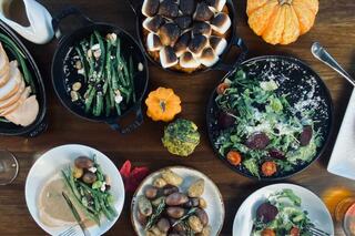 A festive table spread featuring roasted turkey, various colorful side dishes, fresh salad, and decorative pumpkins.