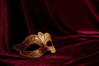 A decorative gold mask rests on rich burgundy fabric, showcasing intricate patterns and a touch of elegance.