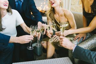 A lively gathering with friends, celebrating and toasting with champagne, smiles, and elegant attire, set against a warm fireplace backdrop.