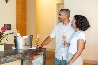 A cheerful couple enjoys celebratory drinks near an ice bucket, sharing smiles in a bright, modern setting accented by a floral arrangement.
