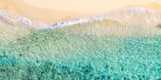 A tranquil shoreline with clear turquoise waters gently lapping against soft sandy beaches under bright sunlight.