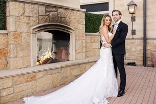 A happy couple embraces in a romantic setting, featuring a beautifully detailed wedding dress, a tuxedo, and a cozy fireplace backdrop.