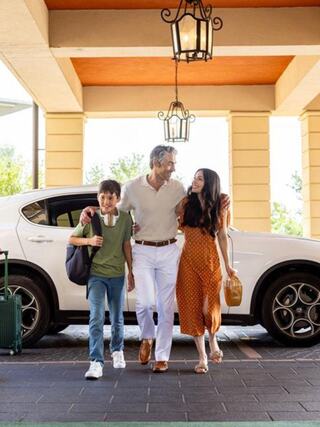 A man walks with a woman and a boy, smiling and enjoying their time together near a white car and a warm, welcoming setting.