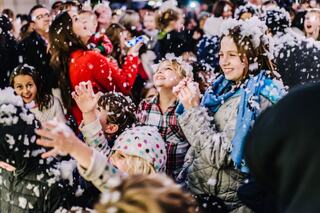 A joyful crowd of children revels in falling foam, laughter and excitement filling the air as they play amidst the whimsical scene.