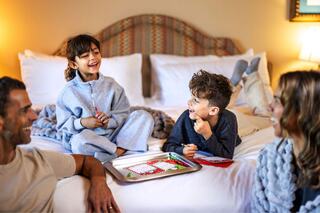 A family enjoys a cozy moment together on a bed, sharing laughs and creativity while decorating cookies. Joy and warmth fill the room.