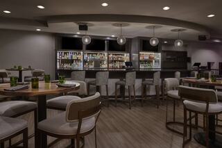 A stylish bar area features modern seating, well-stocked shelves of liquor, ambient lighting, and a cozy atmosphere for socializing.