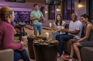 A group of friends enjoys drinks and snacks while bowling, sharing laughter and good times in a vibrant atmosphere.