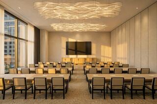 A modern conference room featuring rows of tables and chairs, bathed in warm light from large windows and a striking ceiling design.