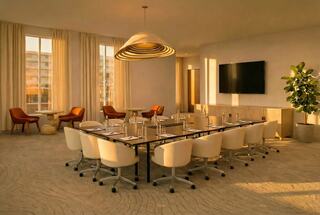 A modern conference room features a long table with chairs, warm lighting, a TV, and plants, creating a welcoming atmosphere for meetings.