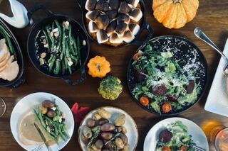 A festive dinner spread featuring green beans, salad, roasted potatoes, and a sweet dessert topped with marshmallows, adorned with mini pumpkins.
