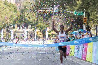 A runner crosses the finish line, arms raised in triumph, as colorful confetti falls and a cheering crowd celebrates the victory.
