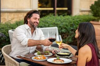 A couple enjoys a romantic dinner outdoors, clinking glasses of wine amidst a beautifully set table with delicious dishes.