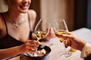 Two people toast with wine glasses, smiling joyfully over a dinner table with a bowl of food, capturing a moment of celebration and connection.