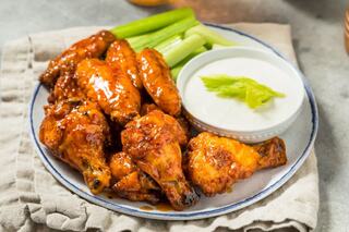 A plate of golden, saucy chicken wings accompanied by celery sticks and a small bowl of creamy dip. Perfect for snacking or sharing!