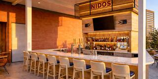 A stylish bar with a marble countertop, high stools, and a well-stocked shelf, bathed in warm sunset light, creates a welcoming atmosphere.